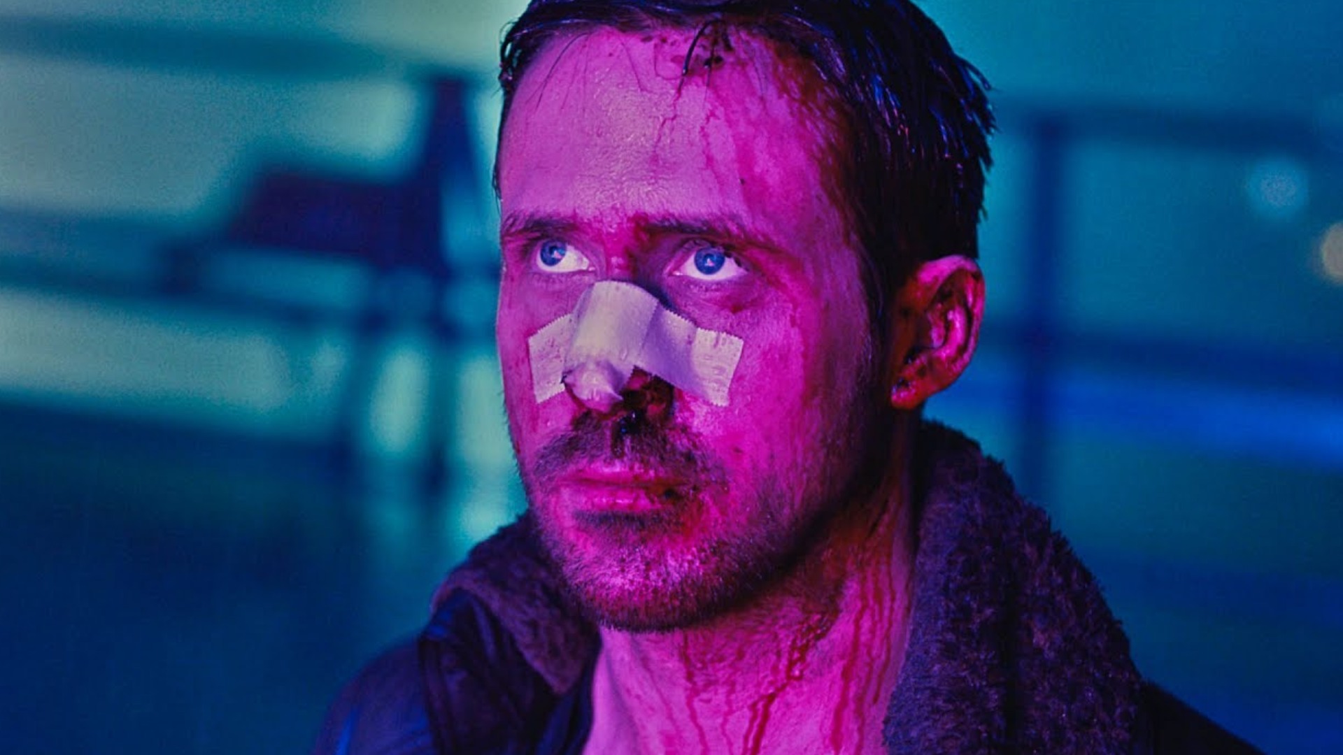 Ryan Gosling as Officer K in Blade Runner 2049, face bloodied, beige bandage on his nose, neon pink and blue light.