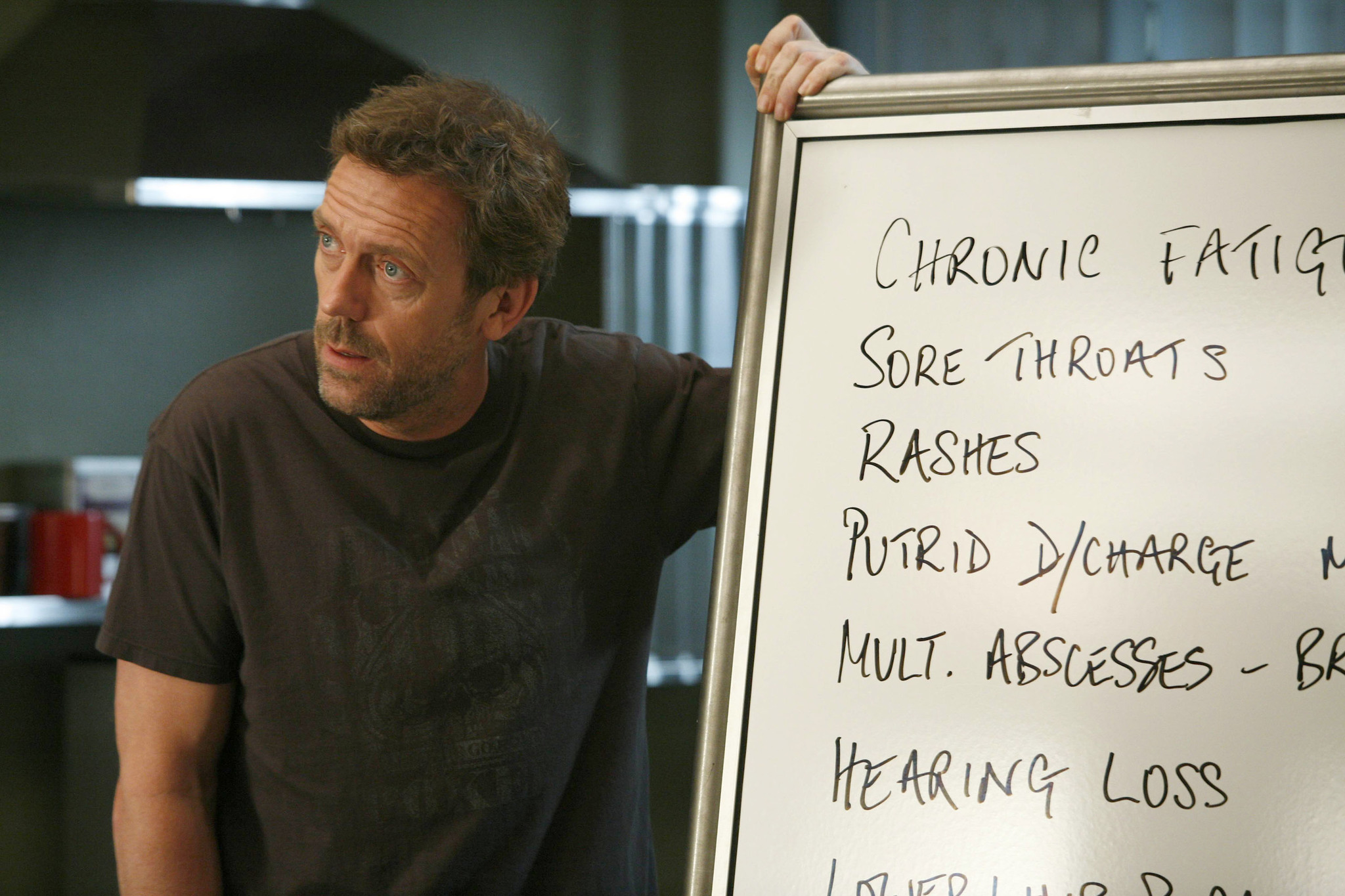 Hugh Laurie as Dr. Gregory House in a dark t-shirt, standing next to a whiteboard of symptoms including chronic fatigue and rashes.